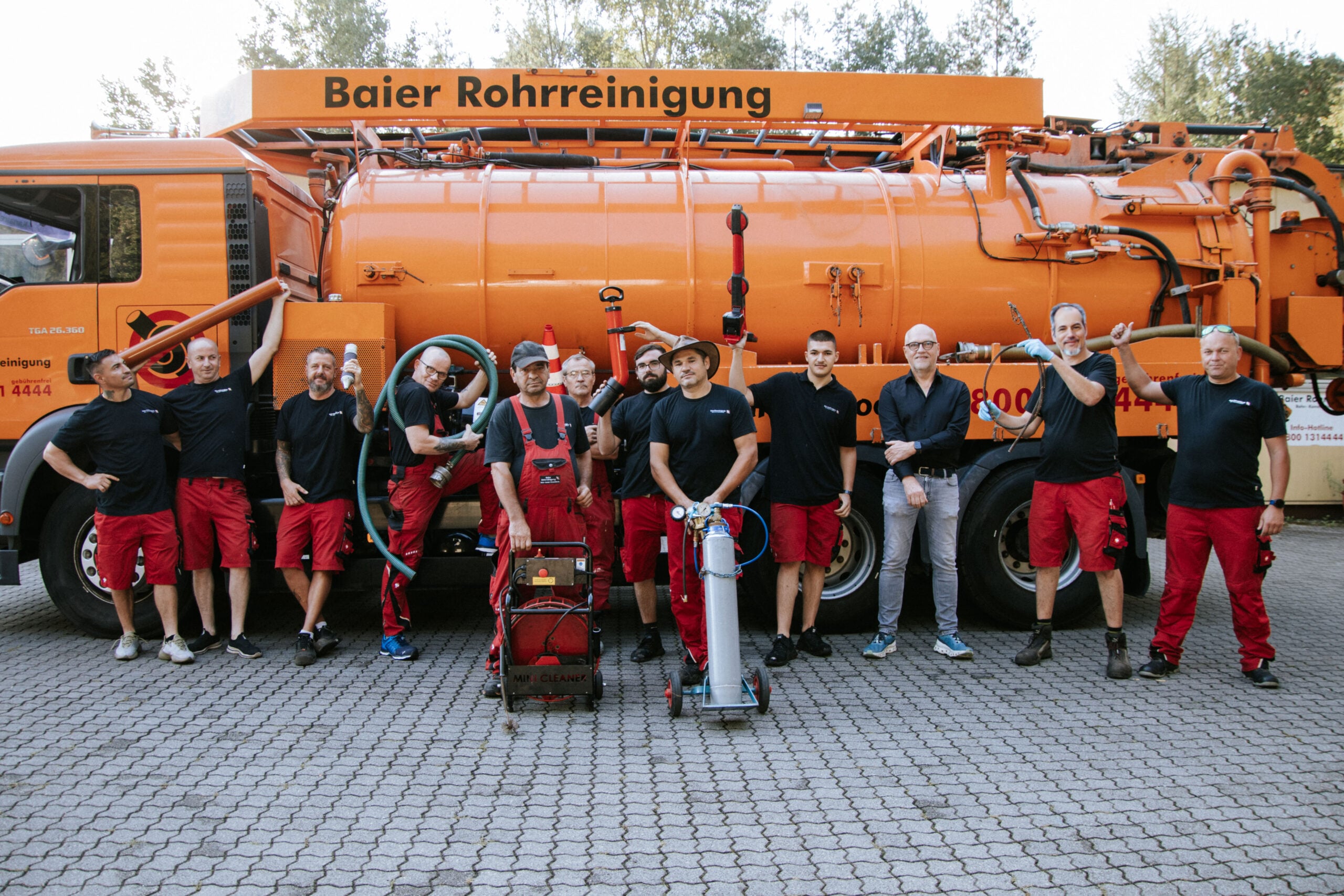 Team der Baier Rohrreinigung vor den orangefarbenen Saug- und Spülfahrzeugen